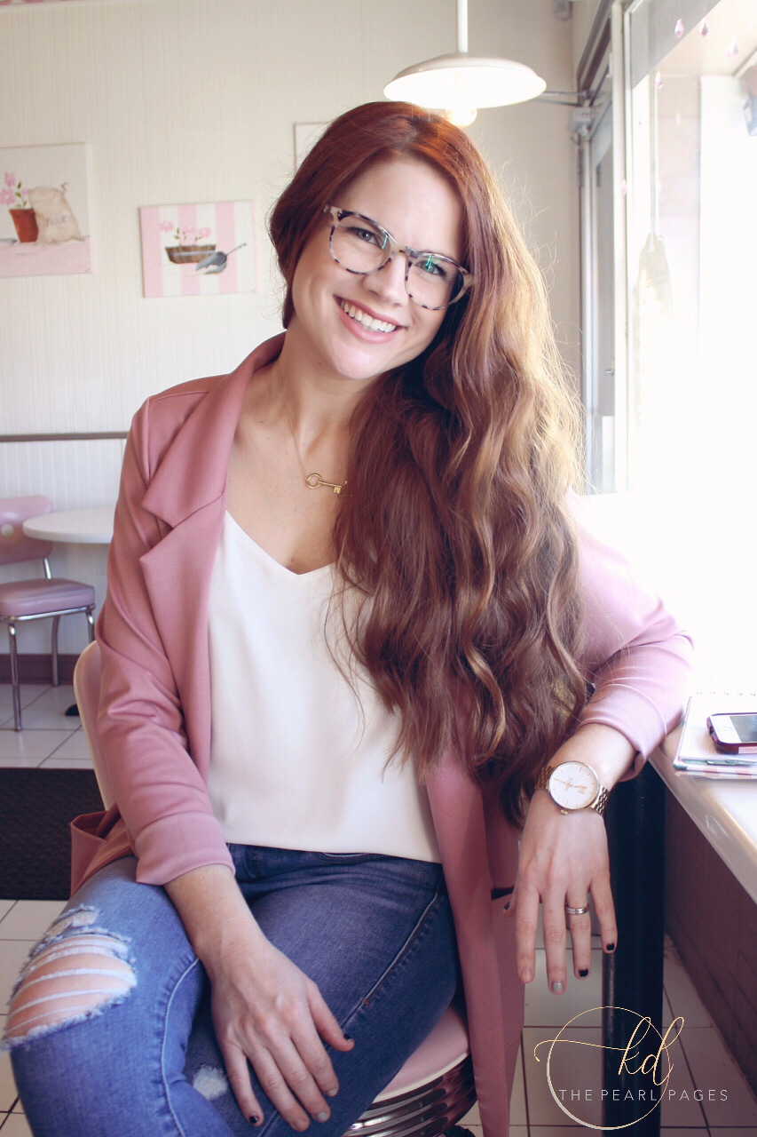 Katie Dunlavy, Lularoe boutique owner, of The Pearl Pages sitting on a stool smiling wearing jeans and a white top with a light pink blazer.