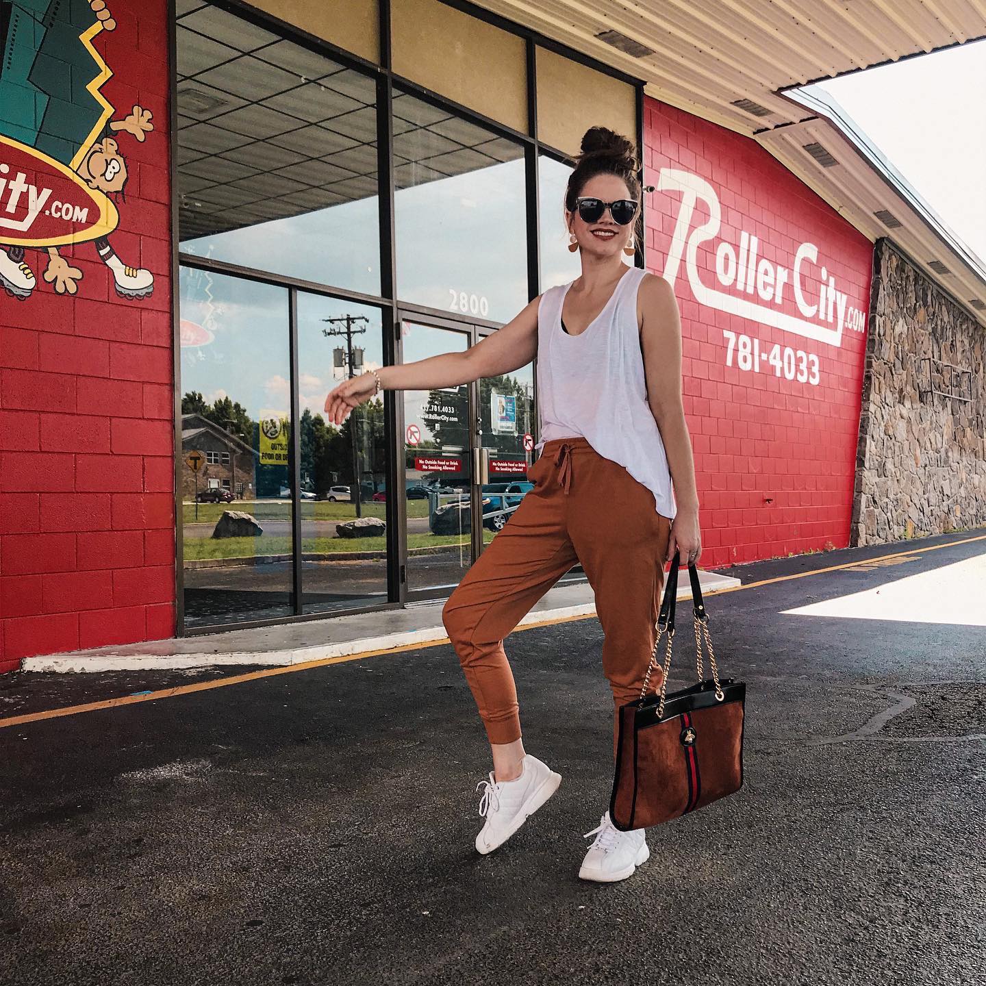 Katie Dunlavy of the Pearl Pages standing in front of Roller City wearing rust colored Lularoe Jax joggers, and white tank top, and oversized sunglasses with her hair in a bun carrying a Gucci tote bag.